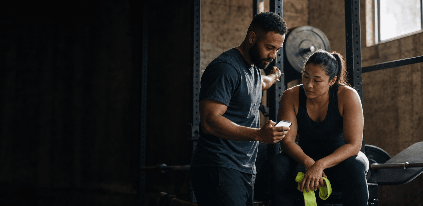 A coach and athlete reviewing a workout on a phone between sets